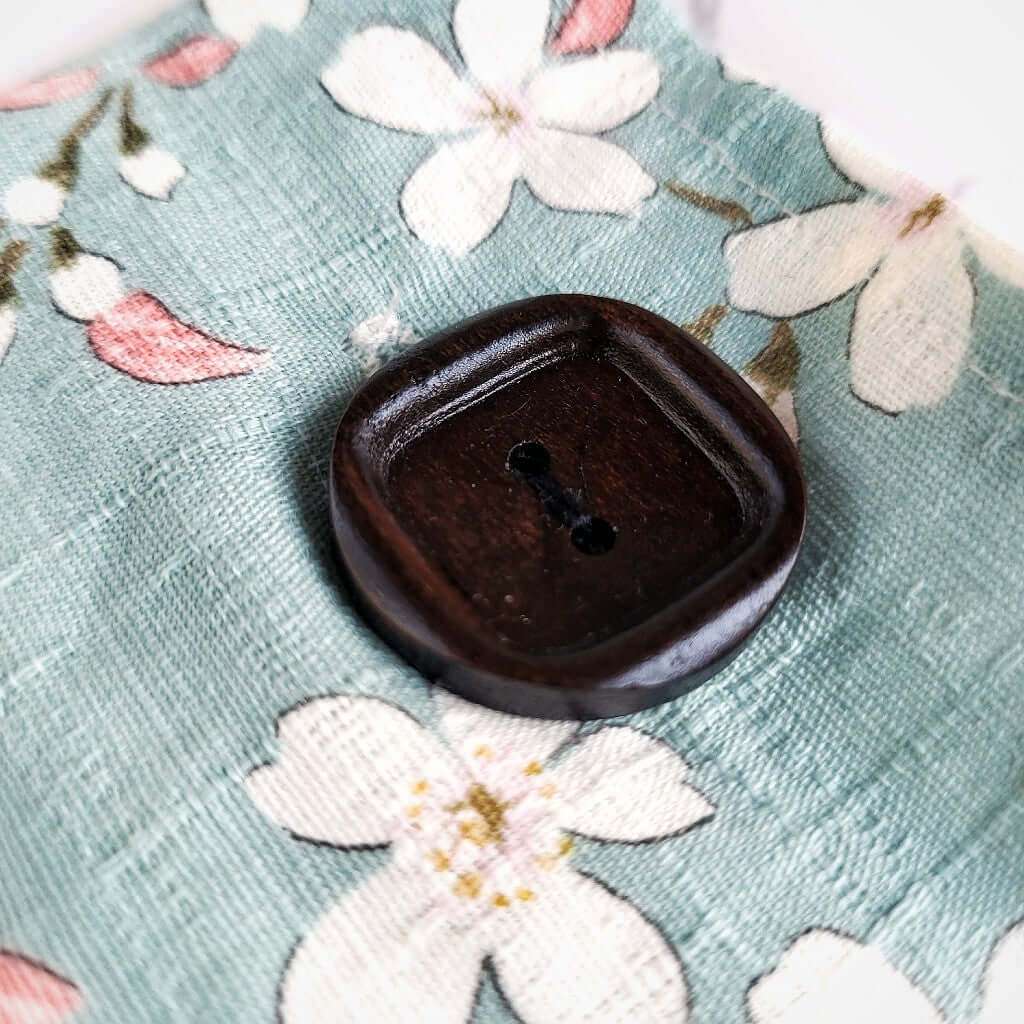 Dettaglio bottone in legno. Cuscino rilassante per occhi eye pillow realizzato in cotono 100%, sfoderabile e lavabile, con ingredienti naturali antinfiammatori, rigeneranti e rilassanti. Stoffa ciliegio in fiore