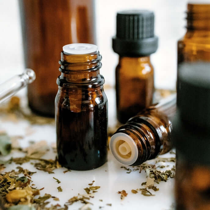 Boccetta ambrata con contagocce in primo piano e altre sullo sfondo, per contenere fragranze per candele profumate o oli essenziali. E' usata er il prodotto Experience Box, Kit Materia Prima Fragranze per candele fai da te.