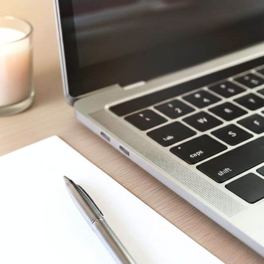 Computer Notebook Portatile con foglio bianco vicino e penna. Sullo sfondo una candela profumata. Immagine per il prodotto digitale Candle Strategy, il primo e unico strumento professionale in Italia rivolto a Candle Maker Hobbisti e Artigiani Professionisti. Un sistema veloce e affidabile per calcolare prezzo e profitto netto di candele artigianali e profumate.