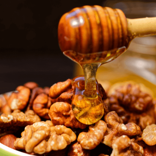 Cucchiaio in legno con miele che cola su di un letto di noci sgusciate, per indicare la fragranza per candele Miele e Noci.