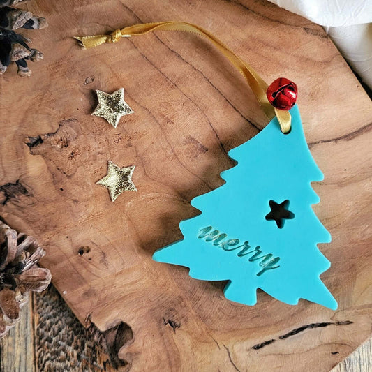 Tartina Profuma Armadi e Cassetti in cera di soia naturale al profumo di Pino. È a forma di Albero di Natale e Decorata con campanellino rosso. Scritta Merry di Merry Christmas.